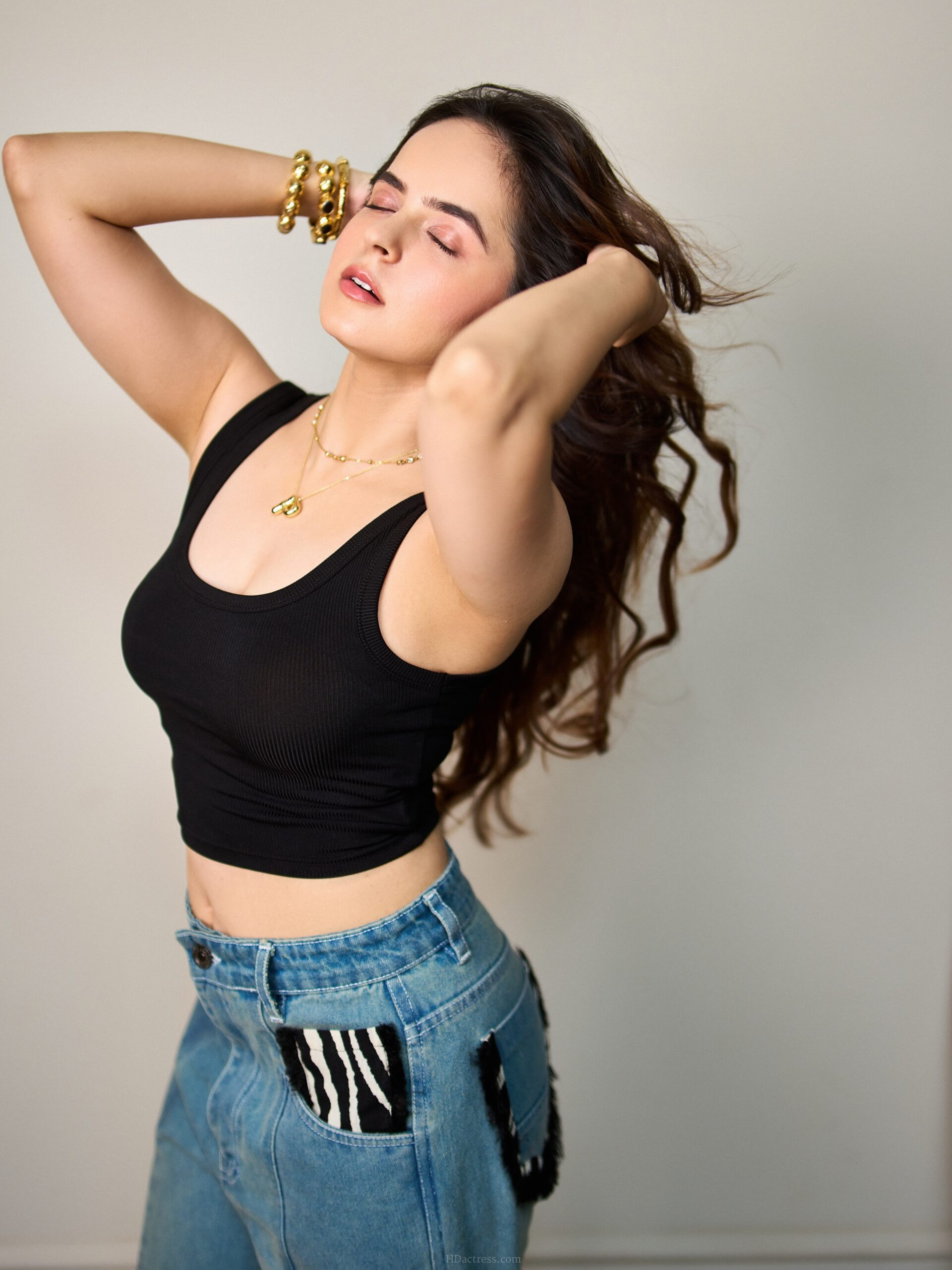 Palak Sindhwani wearing a black ribbed fitted crop tank top with a scoop neckline while posing by a glass door.