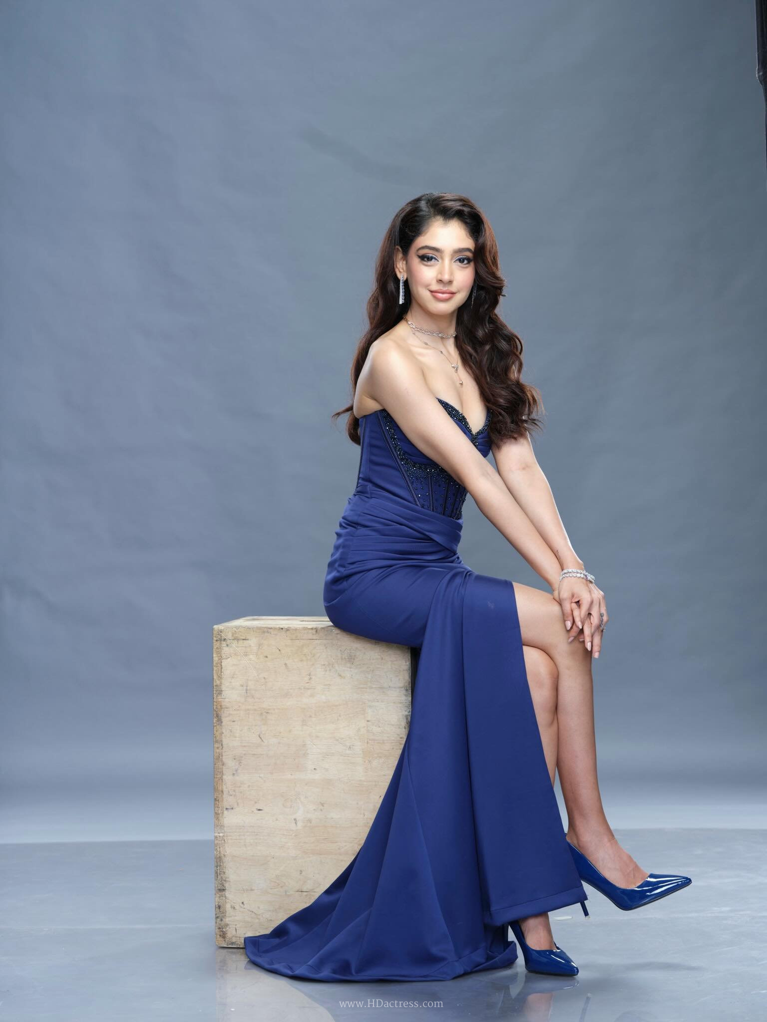 Niti Taylor posing elegantly in a structured, strapless navy blue corset dress with a cinched waistline and flowing satin skirt.