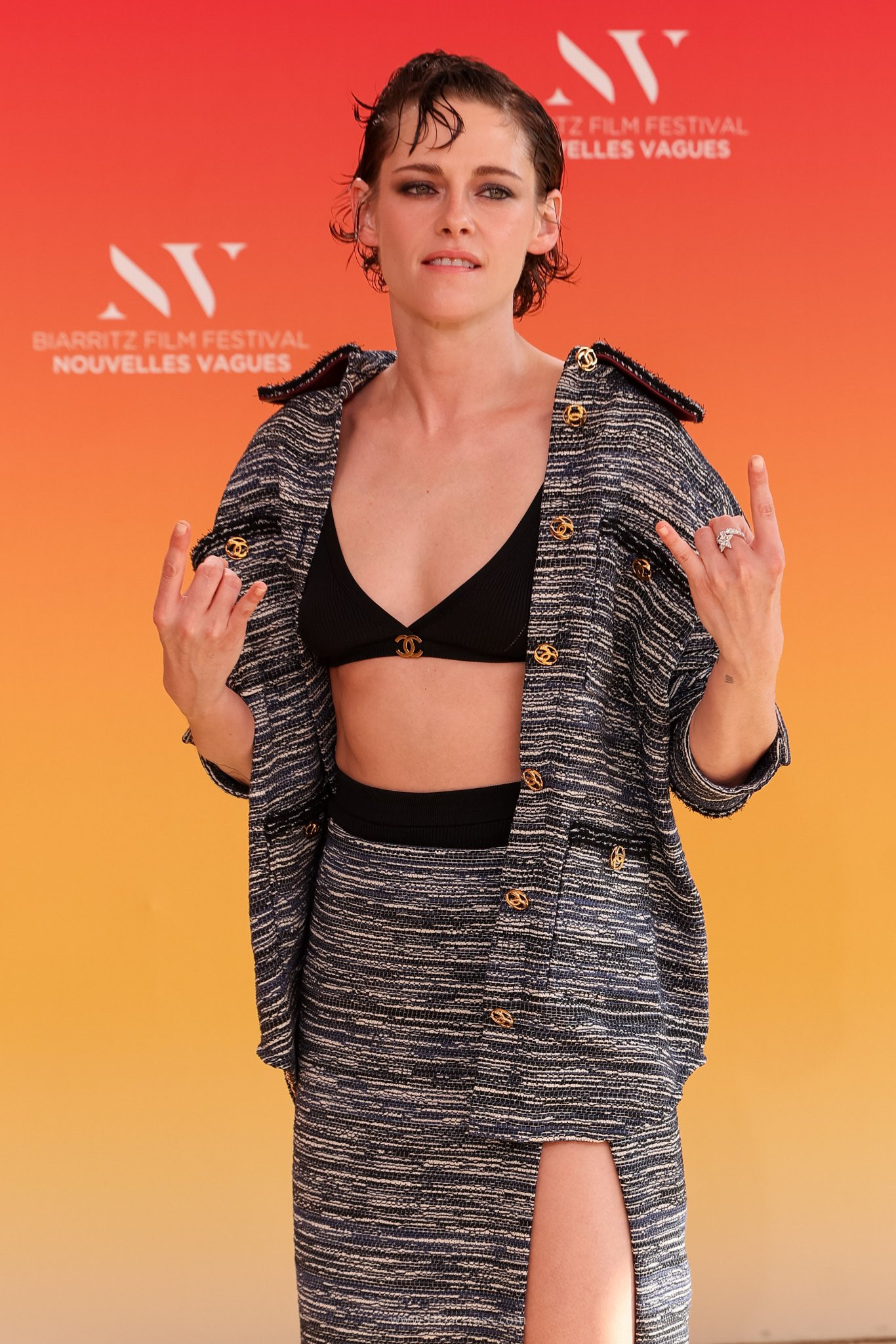 Kristen Stewart showing her toned midriff in a black Chanel bra top under a matching unbuttoned tweed shirt and high-slit skirt at the Biarritz Film Festival.