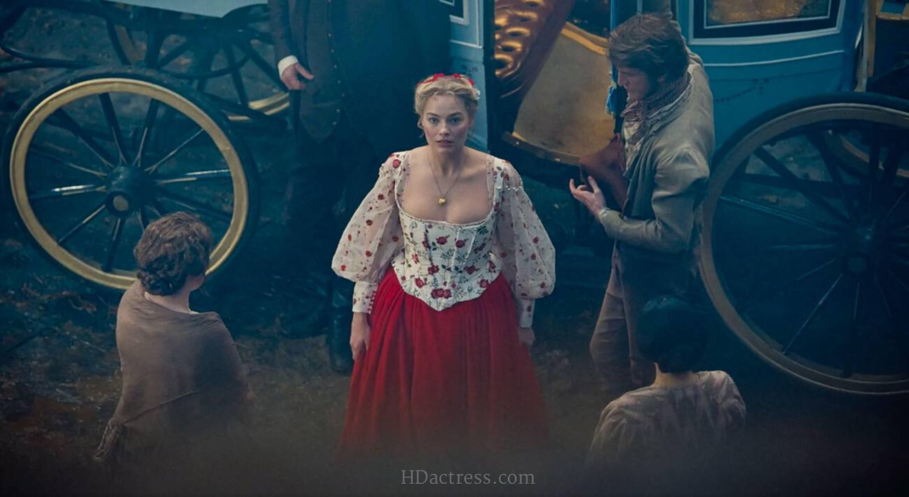 Full length shot of Margot Robbie in a flowing scarlet red gown standing passionately next to Jacob Elordi against a stormy backdrop in the 2026 Wuthering Heights film.