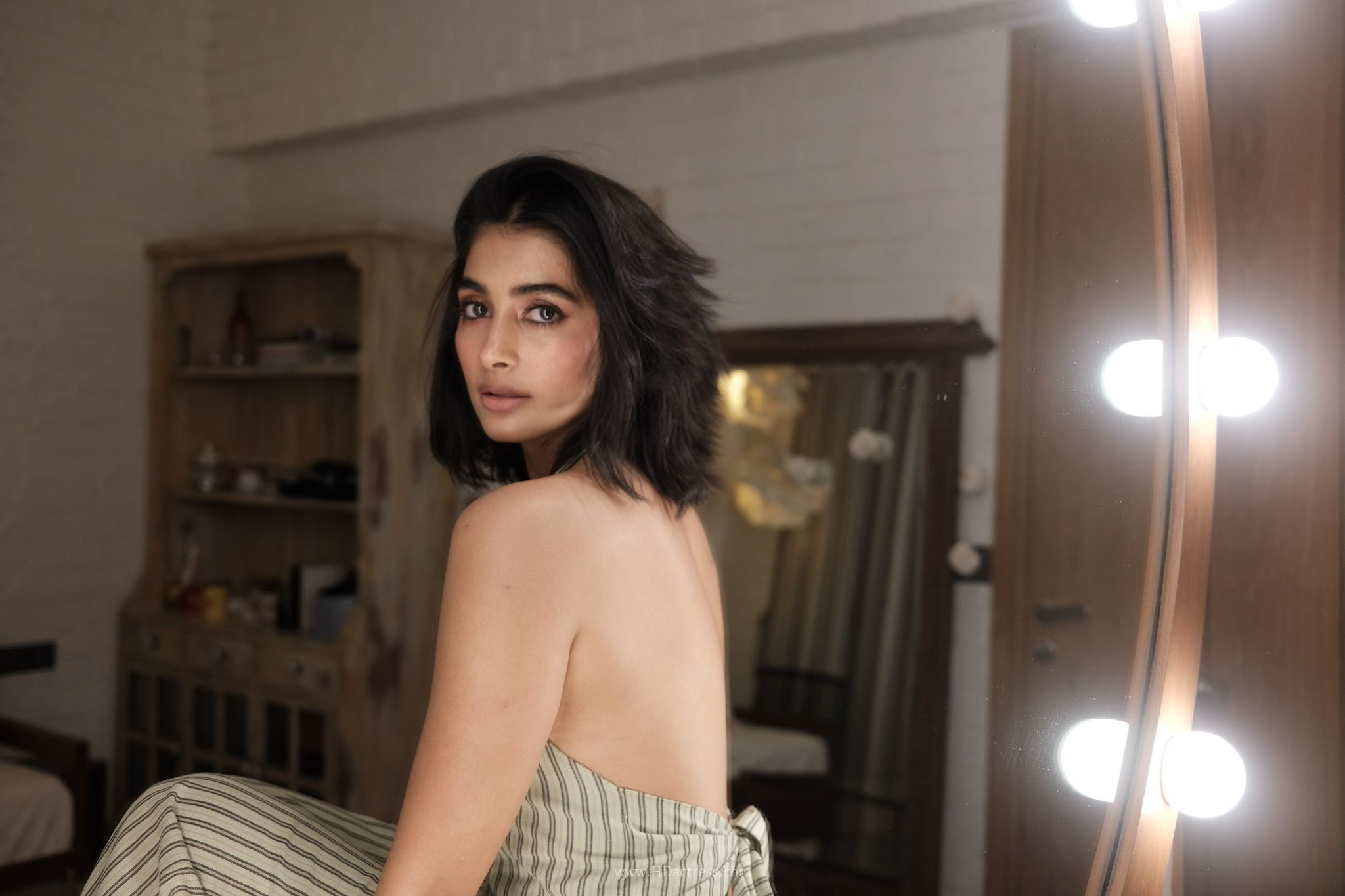 Bollywood actress Pooja Hegde posing gracefully on a sofa showing her bare back in a designer backless gown.